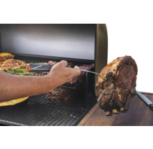 Un homme vérifie la température à cœur d'un morceau de viande sur un gril avec un thermomètre de grill