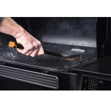 Une personne nettoie la grille d'un gril avec une brosse pour barbecue.