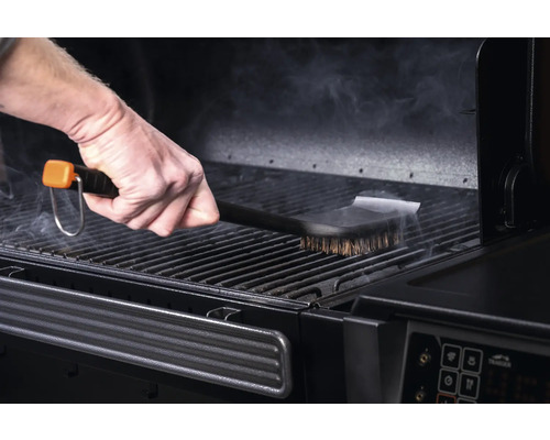 Une personne nettoie la grille d'un gril avec une brosse pour barbecue.