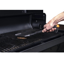 Une brosse à barbecue nettoie une grille de barbecue.