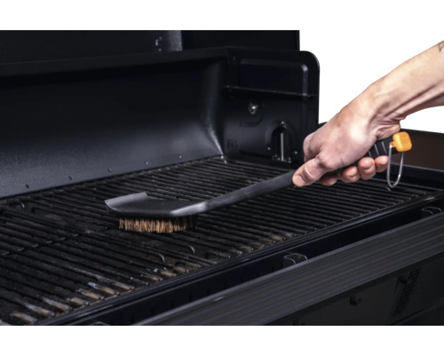 Une brosse à barbecue nettoie une grille de barbecue.