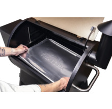 Une personne place un bac de récupération des graisses Traeger dans un barbecue à pellets Traeger.