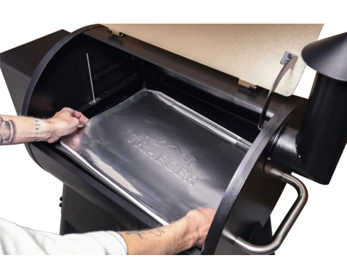 Une personne place un bac de récupération des graisses Traeger dans un barbecue à pellets Traeger.