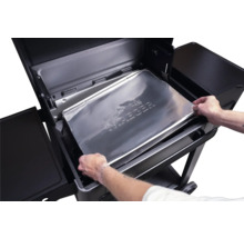 Mains plaçant une protection de plateau d égouttement en aluminium Traeger dans un barbecue à pellets Traeger noir.