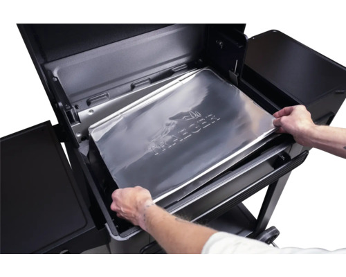 Une personne place un tapis de barbecue avec le logo Traeger dans un barbecue Traeger.