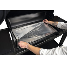 Mise en place d une feuille de protection en aluminium sur mesure de Traeger dans le bac à graisse d un barbecue à pellets.