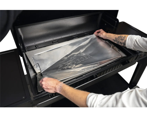 Mise en place d une feuille de protection en aluminium sur mesure de Traeger dans le bac à graisse d un barbecue à pellets.