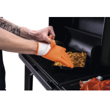 Utilisation d'un gant de barbecue en silicone orange résistant à la chaleur sur un gant en tissu blanc devant un barbecue avec un plat.