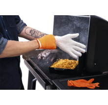 Personne portant un gant de barbecue résistant à la chaleur pendant la cuisson de viande et d'un accompagnement dans un fumoir.