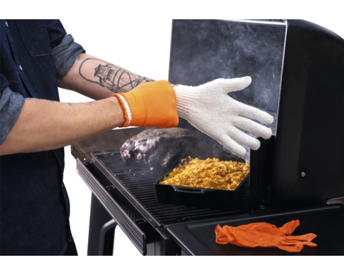 Personne portant un gant de barbecue résistant à la chaleur pendant la cuisson de viande et d'un accompagnement dans un fumoir.