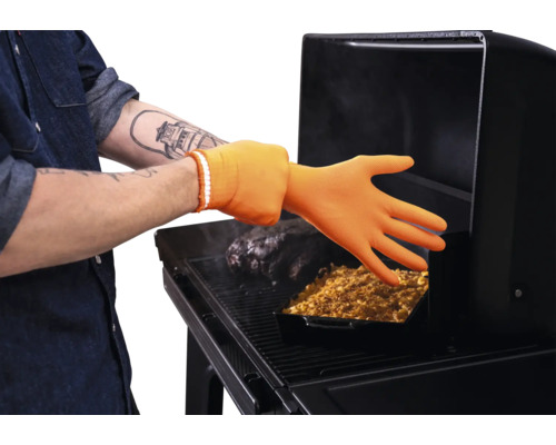 Gant de barbecue résistant à la chaleur en silicone utilisé sur un barbecue avec de la viande et un plat à four.