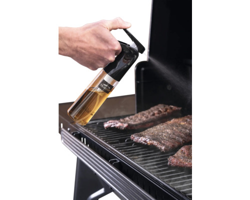 Main vaporisant de l'huile sur de la viande sur un barbecue avec un vaporisateur Traeger. Traeger Logo.