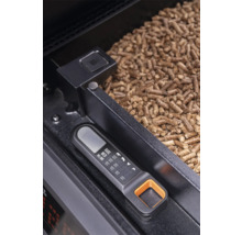 Thermomètre numérique Traeger avec guide de température pour viandes à côté de granulés de bois dans le réservoir d'un barbecue à pellets.