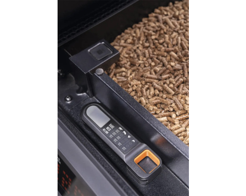 Thermomètre numérique Traeger avec guide de température pour viandes à côté de granulés de bois dans le réservoir d'un barbecue à pellets.
