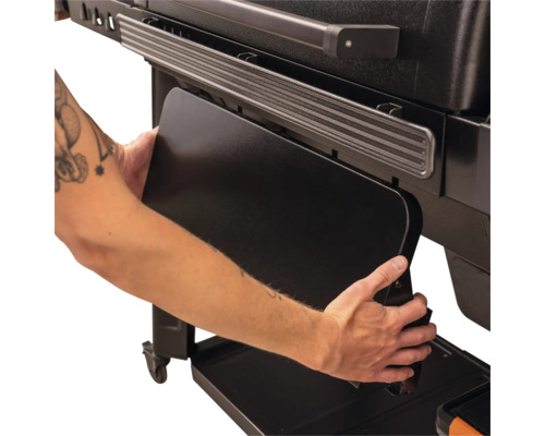 Klappbare Seitenablage eines schwarzen Grills wird per Hand nach unten geklappt.