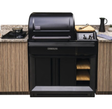 Gril à granulés Traeger Timberline intégré dans une cuisine d'extérieur avec des meubles en bois, un plan de travail en pierre et une plaque à induction.