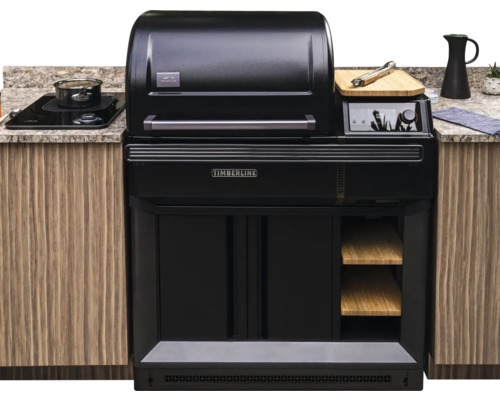Gril à granulés Traeger Timberline intégré dans une cuisine d'extérieur avec des meubles en bois, un plan de travail en pierre et une plaque à induction.