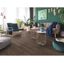 Wohnzimmer mit dunklem Boden in Holzoptik, grauem Sofa, blauem Sessel und grüner Wand mit Zimmerpflanzen. Modern und hell gestaltet.