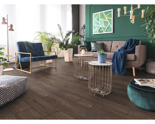 Wohnzimmer mit dunklem Boden in Holzoptik, grauem Sofa, blauem Sessel und grüner Wand mit Zimmerpflanzen. Modern und hell gestaltet.