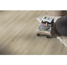 Laminatboden in heller Eichen-Optik in einem wohnlichen Raum mit hellem Fellteppich, Poufs und Büchern auf einem Rollbrett.