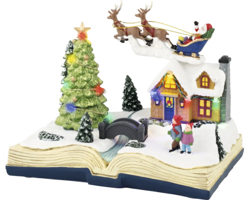 Décoration de Noël en forme de livre ouvert avec scène d'hiver enneigée, maison éclairée, sapin de Noël et Père Noël dans son traîneau.