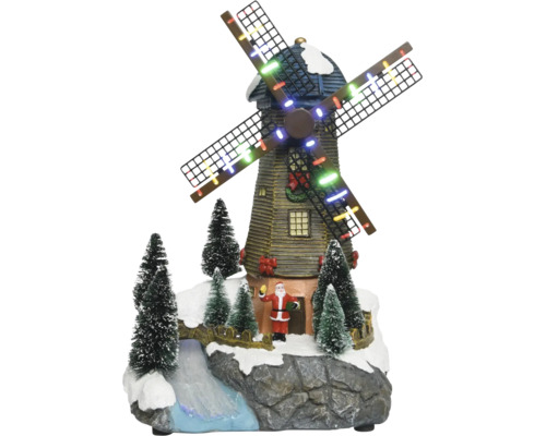 Décoration de Noël avec moulin à vent illuminé, figurine du Père Noël, sapins enneigés et ruisseau sur un socle rocheux.