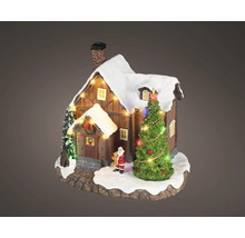 Maison miniature de Noël en bois avec toit enneigé, sapin illuminé et petite figurine de Père Noël.