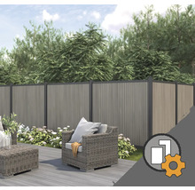 Clôture de protection en WPC dans un jardin avec terrasse en bois, meubles de salon gris et plantes à fleurs devant des arbres.