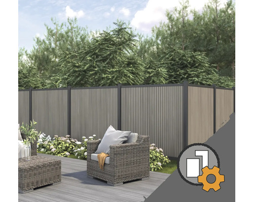 Clôture de protection en WPC dans un jardin avec terrasse en bois, meubles de salon gris et plantes à fleurs devant des arbres.