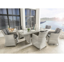Salon de jardin en résine tressée claire avec table en verre et six fauteuils incluant des coussins sombres sur une terrasse avec vue mer.