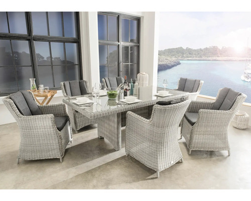 Salon de jardin en résine tressée claire avec table en verre et six fauteuils incluant des coussins sombres sur une terrasse avec vue mer.