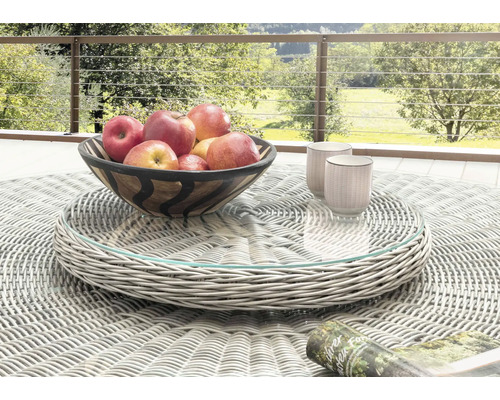 Plateau tournant lumineux en résine tressée grise avec plateau en verre sur une table de jardin ronde avec bol de fruits et tasses à l'extérieur.