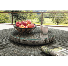 Table de jardin ronde en résine tressée grise avec plateau en verre, avec une coupe de pommes et des tasses sur une terrasse avec vue sur la nature.
