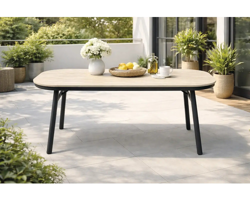 Table de jardin moderne sur une terrasse avec plateau en aspect bois et structure en métal noir, entourée de plantes.