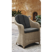 Fauteuil de jardin tressé avec coussins d'assise et de dossier sur une terrasse en pierre devant un mur rustique avec des plantes.