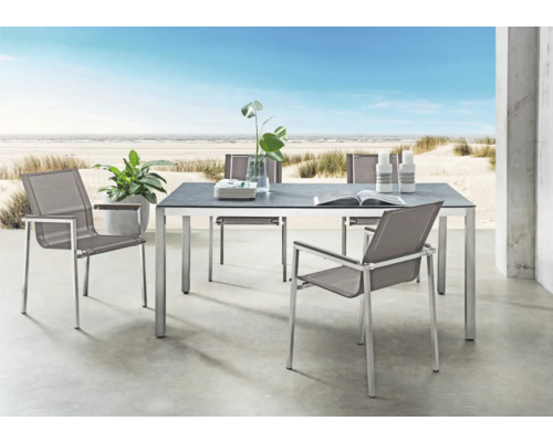 Ensemble mobilier de jardin moderne avec table rectangulaire et quatre chaises sur terrasse vue mer. Table avec plateau foncé et cadre en métal.