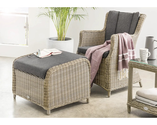 Ensemble moderne de fauteuil, pouf et table d'appoint en rotin synthétique avec coussins dans un espace lumineux et spacieux avec une plante.