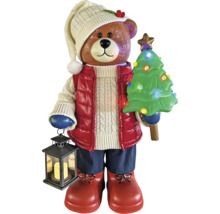 Ours de Noël avec sapin illuminé et lanterne, portant un bonnet en tricot, une veste et des bottes.