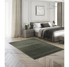 Dunkelgrüner Hochflor-Teppich auf hellem Fischgrätparkett in einem modernen, hellen Schlafzimmer mit Bett und Nachttisch.