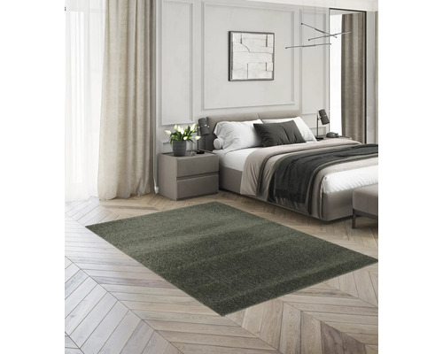 Dunkelgrüner Hochflor-Teppich auf hellem Fischgrätparkett in einem modernen, hellen Schlafzimmer mit Bett und Nachttisch.