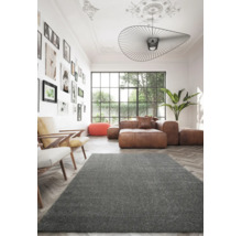 Moderner Wohnraum mit grauem Hochflor-Teppich, braunem Ledersofa, Fischgrät-Parkett und Bilderwand vor großem Fenster.