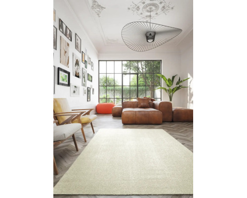 Modernes, helles Wohnzimmer mit hellem Teppich auf Fischgrätparkett, braunem Ledersofa, zwei Sesseln und grosser Fensterfront.