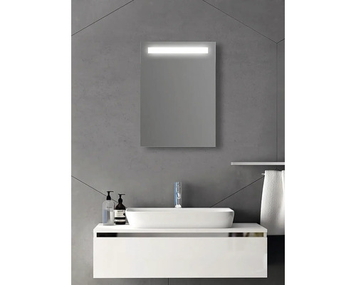 Miroir de salle de bain rectangulaire avec éclairage LED intégré au-dessus d'un lavabo et d'un meuble sous-vasque blancs sur mur gris.