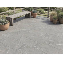 Dalles de terrasse aspect pierre avec marbrures grises sur une terrasse avec banc en bois et pots de fleurs à l'extérieur.