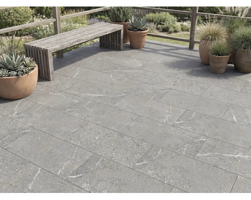 Dalles de terrasse aspect pierre avec marbrures grises sur une terrasse avec banc en bois et pots de fleurs à l'extérieur.