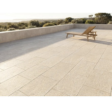 Moderne Terrasse mit grossen Steinplatten, einer Holzsonnenliege und einer Steinmauer mit Blick auf eine Landschaft und das Meer.