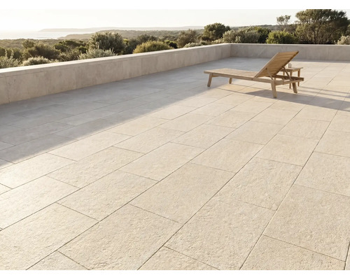 Moderne Terrasse mit grossen Steinplatten, einer Holzsonnenliege und einer Steinmauer mit Blick auf eine Landschaft und das Meer.