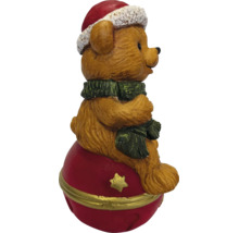 Weihnachtsfigur Teddybär mit Weihnachtsmütze und Schal sitzend auf einer roten Weihnachtskugel mit goldenem Stern.