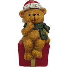 Weihnachts-Teddybär mit Nikolausmütze und Schal auf einem Geschenkpaket sitzend