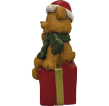 Weihnachtsfigur brauner Bär mit roter Nikolausmütze und grünem Schal sitzend auf einem roten Geschenkpaket.
